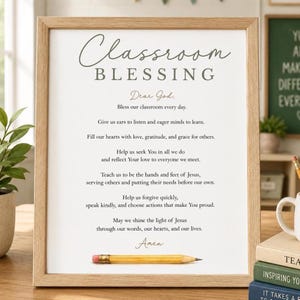May include: A framed print titled Classroom Blessing with dark grey text on a white background. The prayer includes lines about listening, learning, and love, ending with Amen. A yellow pencil is placed horizontally across the bottom of the print.