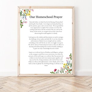May include: A framed wall art print titled Our Homeschool Prayer, featuring black text on a white background. The design is decorated with watercolor illustrations of colorful wildflowers in the top left and bottom right corners, set in a light wood frame.