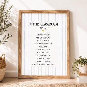Könnte beinhalten: Ein gerahmter Wandkunstdruck mit weißem Hintergrund und vertikalen hellblauen Streifen. Der Text lautet: IN THIS CLASSROOM we [Kreuzsymbol] GLORIFY GOD, ASK QUESTIONS, WORK HARD, BUILD CHARACTER, FORGIVE, ARE GRATEFUL, KEEP TRYING, SERVE OTHERS, PLAY OUTSIDE, LOVE TO READ, ARE ALWAYS LEARNING.