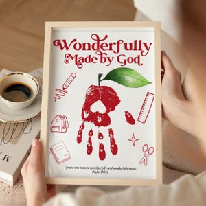 May include: A framed print with the words "Wonderfully Made by God" in red script. The artwork features a red handprint shaped like an apple, with a green leaf, and school-themed illustrations. The text "I praise you because I am fearfully and wonderfully made Psalm 139:14" is at the bottom.