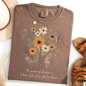 May include: A brown t-shirt with a floral design and the text "The purpose of education is to know God and to make him known."