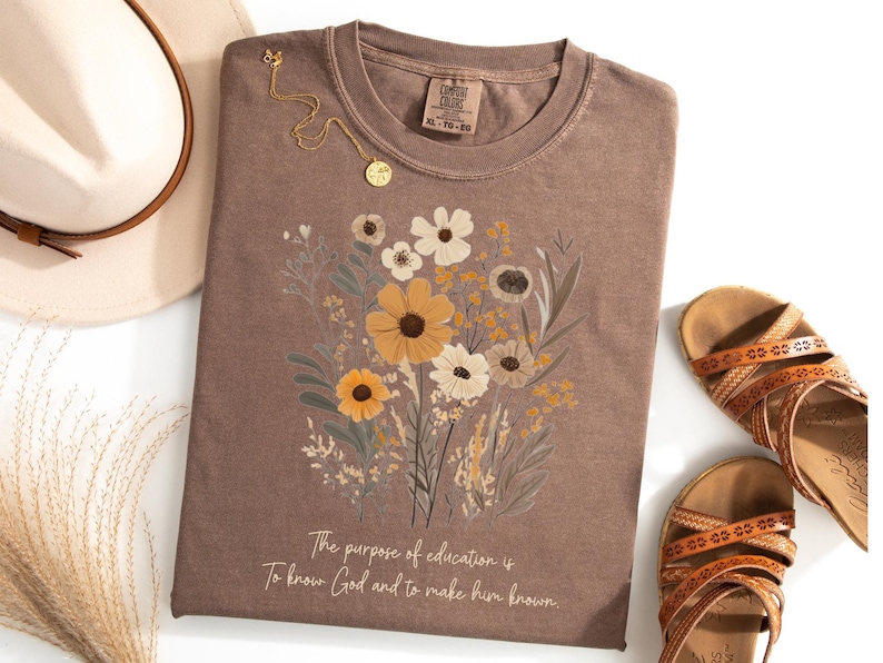 May include: A brown t-shirt with a floral design and the text "The purpose of education is to know God and to make him known."