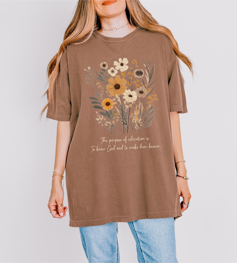 May include: A brown oversized t-shirt with a floral design and the text "The purpose of education is to know God and to make him known."