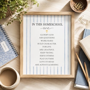 May include: A framed wall art print featuring a light blue vertical striped background with the black text IN THIS HOMESCHOOL WE, a small yellow cross, and a list of values including GLORIFY GOD, ASK QUESTIONS, WORK HARD, and ARE ALWAYS LEARNING.