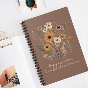 Può includere: Un quaderno a spirale marrone con un disegno floreale e la citazione "Lo scopo dell'educazione è conoscere Dio e farlo conoscere."