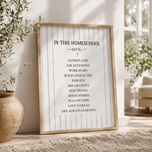 May include: A framed wall art print featuring a white background with vertical light blue stripes. The text reads: IN THIS HOMESCHOOL WE, followed by a small yellow cross and a list of values including GLORIFY GOD, ASK QUESTIONS, and ARE ALWAYS LEARNING.