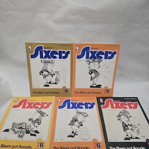 May include: A collection of vintage Philadelphia 76ers basketball program booklets. Each booklet features the team's logo, the word "Seventy Sixers", and a cartoon illustration of a colonial-era figure. The booklets are in various colors.