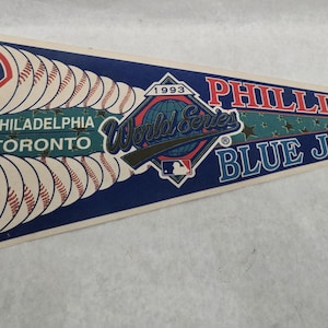 May include: A vintage pennant featuring the Philadelphia Phillies and Toronto Blue Jays. The pennant is blue, white, and red, with baseball imagery and text that reads "1993 World Series." The pennant is approximately 12 inches long.