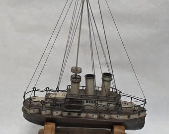 May include: A vintage model ship with a brown hull and white accents, mounted on a wooden stand. The ship features three smokestacks, a central mast, and intricate rigging details. The model is a detailed representation of a classic vessel.