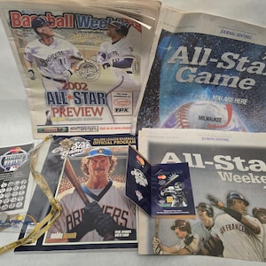 May include: A collection of baseball-themed memorabilia, including newspapers and programs. The items feature the Brewers and the 2002 All-Star Game, with text such as "All-Star Game" and "Preview".
