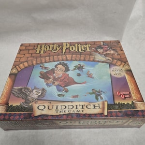 May include: A rectangular board game box titled Harry Potter Quidditch The Game. The box features an illustration of characters flying on broomsticks, an owl, and a brick archway. It indicates 2 to 14 players, ages 8 and up, by University Games.