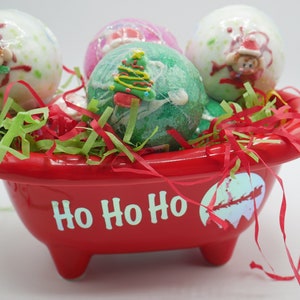 Könnte beinhalten: Eine rote Badewanne mit dem Text "Ho Ho Ho" auf der Vorderseite. Die Badewanne ist gefüllt mit bunten Badebomben, die mit Weihnachtsmotiven verziert sind, darunter ein Weihnachtsbaum, ein Schneemann und ein Weihnachtsmann.