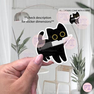Op de afbeelding: Een zwarte kattensticker met gele ogen en een mes. De sticker wordt door een hand vastgehouden. Tekst op de sticker zegt "pinkindigoco". Extra tekst luidt "controleer de beschrijving voor sticker afmetingen" en "ALLE BESTELLINGEN WORDEN GELEVERD MET EEN MINI!"