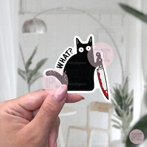 Op de afbeelding: Zwarte kat sticker met een mes en de tekst "WHAT?" in wit. De kat heeft een verraste uitdrukking en houdt het mes in zijn poot.