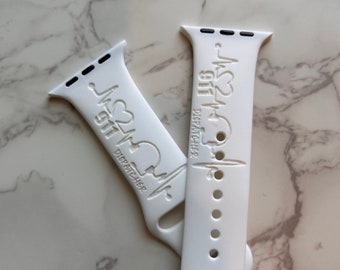 Op de afbeelding: Twee witte Apple Watch-bandjes met de tekst "911 DISPATCHER" en een hartslagontwerp. De bandjes zijn gemaakt van flexibel materiaal en zijn ontworpen voor een standaard Apple Watch. Ze liggen op een wit en grijs marmeren oppervlak.