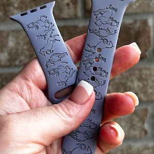 Pode incluir: Duas pulseiras de silicone roxo para Apple Watch com um padrão repetido de cavalos gravados na superfície.