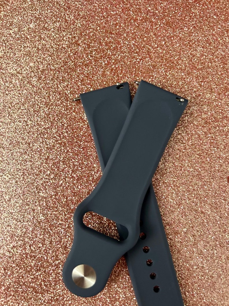 Puede incluir: Dos correas de reloj de silicona gris oscuro con una hebilla plateada. Las correas est&aacute;n cruzadas una sobre la otra.