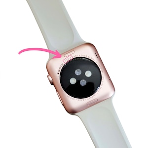Puede incluir: La parte posterior de un Apple Watch Series 7 de color oro rosa con una banda deportiva blanca. La esfera del reloj es negra y tiene una caja de 42 mm.