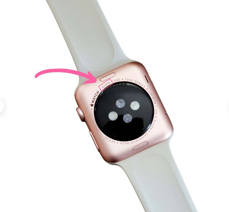 Puede incluir: La parte posterior de un Apple Watch Series 7 de color oro rosa con una banda deportiva blanca. La esfera del reloj es negra y tiene una caja de 42 mm.