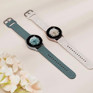 K&ouml;nnte beinhalten: Zwei Smartwatch-Armb&auml;nder mit Blumenmustern. Ein Armband ist wei&szlig; mit einem wei&szlig;en Blumenmuster und das andere ist dunkelblau mit einem blauen Blumenmuster.