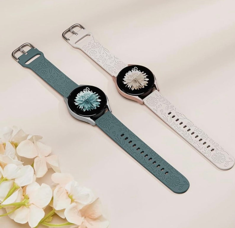 K&ouml;nnte beinhalten: Zwei Smartwatch-Armb&auml;nder mit Blumenmustern. Ein Armband ist wei&szlig; mit einem wei&szlig;en Blumenmuster und das andere ist dunkelblau mit einem blauen Blumenmuster.