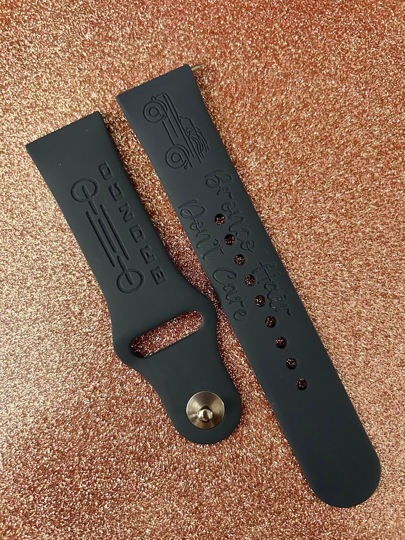 Puede incluir: Dos correas de reloj de silicona negra con dise&ntilde;os grabados. Una correa tiene un peque&ntilde;o dise&ntilde;o de cami&oacute;n y el texto "La aventura te espera, no esperes, explora." La otra correa tiene un dise&ntilde;o de l&iacute;nea con el texto "M&aacute;s all&aacute; de la E."
