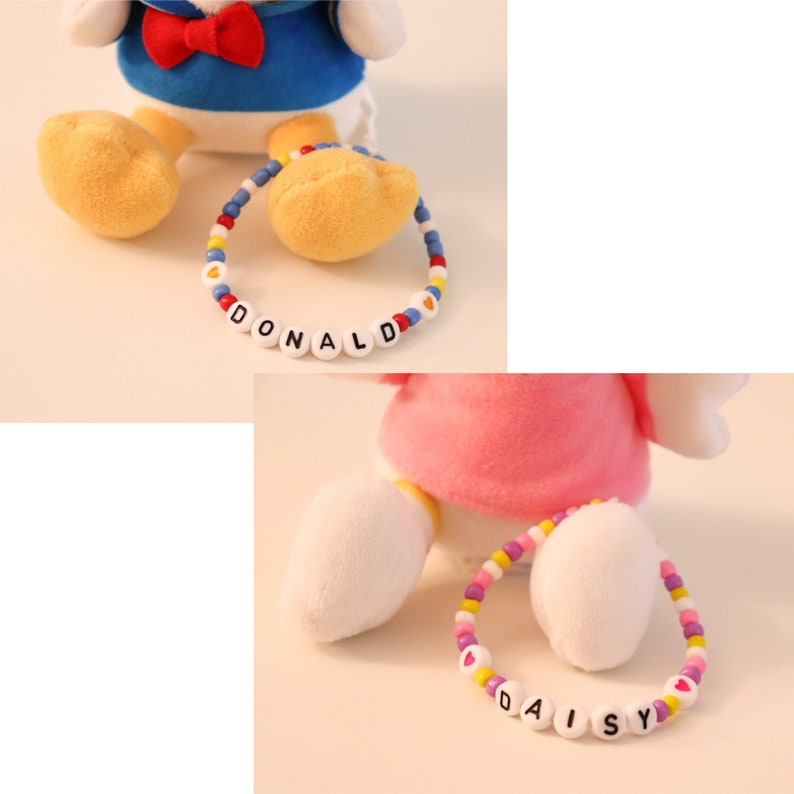 以下が含まれることがあります： 青いぬいぐるみとピンクのぬいぐるみの2つ。カラフルなビーズのブレスレットで「DONALD」と「DAISY」と綴られています。