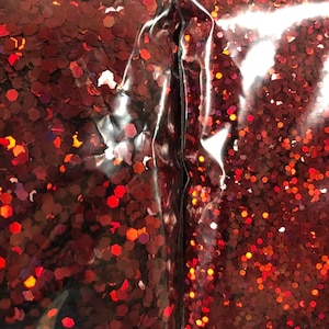 May include: A close-up of a bag of red glitter. The glitter is in a clear plastic bag and is very sparkly.