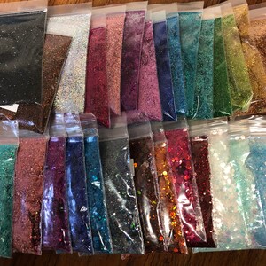 K&ouml;nnte beinhalten: Sortiment von 25 kleinen Beuteln mit Glitter in verschiedenen Farben, darunter Schwarz, Braun, Silber, Rot, Rosa, Blau, Gr&uuml;n, Gold und Wei&szlig;. Der Glitter ist in durchsichtigen Plastikt&uuml;ten verpackt.