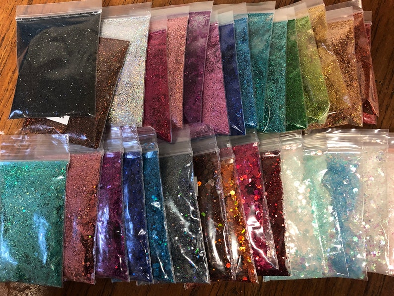 K&ouml;nnte beinhalten: Sortiment von 25 kleinen Beuteln mit Glitter in verschiedenen Farben, darunter Schwarz, Braun, Silber, Rot, Rosa, Blau, Gr&uuml;n, Gold und Wei&szlig;. Der Glitter ist in durchsichtigen Plastikt&uuml;ten verpackt.