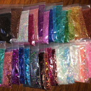 K&ouml;nnte beinhalten: Eine Sammlung von 24 kleinen Beuteln, gef&uuml;llt mit verschiedenen Farben von Glitter. Die Beutel sind in Reihen angeordnet und alle aus durchsichtigem Plastik.