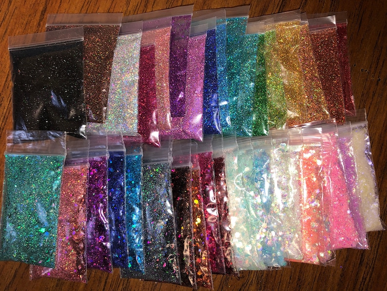 K&ouml;nnte beinhalten: Eine Sammlung von 24 kleinen Beuteln, gef&uuml;llt mit verschiedenen Farben von Glitter. Die Beutel sind in Reihen angeordnet und alle aus durchsichtigem Plastik.