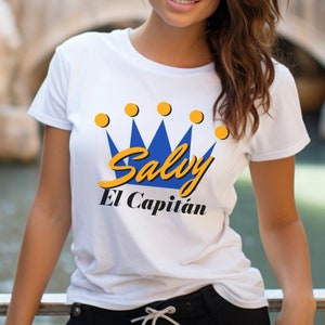May include: White t-shirt with a blue and yellow crown graphic and the text "Salvy El Capitan".