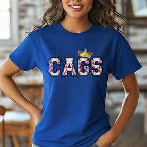 May include: Royal blue t-shirt with the word "CAGS" in baseball-themed lettering, topped with a gold crown. The letters are designed to resemble baseballs, with red stitching. A casual, sporty design.