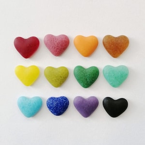 May include: Twelve heart-shaped glass pieces in various colours, including red, pink, orange, brown, yellow, green, blue, purple, and black.