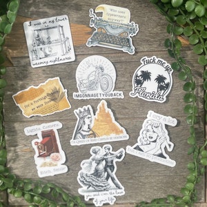 Op de afbeelding: Een verzameling stickers met diverse ontwerpen en tekst. De stickers tonen illustraties van een typemachine, een motorfiets, een vrouw en een dansend stel. Sommige stickers bevatten zinnen als "I cry a lot but I am so productive."