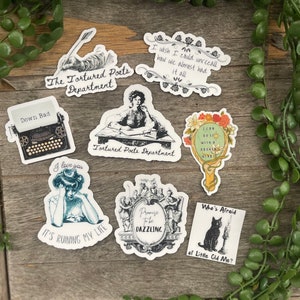 May include: A collection of stickers with various designs and text. The stickers feature illustrations of a typewriter, a woman, a cat, and floral elements. Text includes phrases like "The Tortured Poets Department" and "Who's Afraid of Little Old Me?"