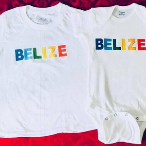 May include: Two white t-shirts with the word "Belize" printed in rainbow colors. The larger shirt has short sleeves and the smaller shirt has long sleeves.