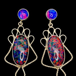 Può includere: Un paio di orecchini color argento con un vivace design in opale multicolore. Ogni orecchino presenta una piccola pietra rotonda blu e rosa nella parte superiore, collegata a un'opale ovale più grande con sfumature rosse, verdi e blu.