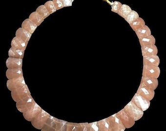 May include: A necklace made of light pink sunstone beads. The beads are faceted and have a slightly iridescent sheen. The necklace is strung on a red cord with gold accents.