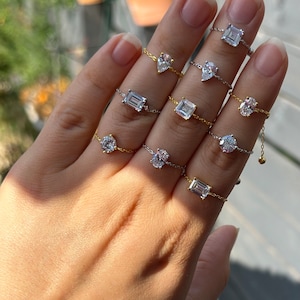 May include: A hand model wearing a variety of delicate gold and silver chain rings with different shaped clear gemstones. The rings are connected by a chain that runs through the fingers.