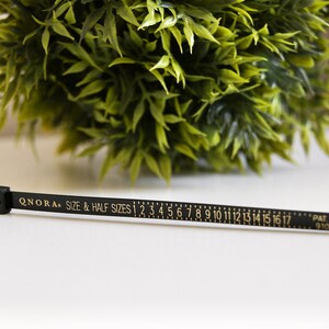Pode incluir: Fita m&eacute;trica preta com letras douradas que dizem "QNORA SIZE & HALF SIZES 1 2 3 4 5 6 7 8 9 10 11 12 13 14 15 16 17 PAT PEND 9101693".
