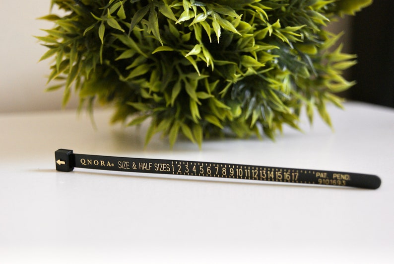 Pode incluir: Fita m&eacute;trica preta com letras douradas que dizem "QNORA SIZE & HALF SIZES 1 2 3 4 5 6 7 8 9 10 11 12 13 14 15 16 17 PAT PEND 9101693".