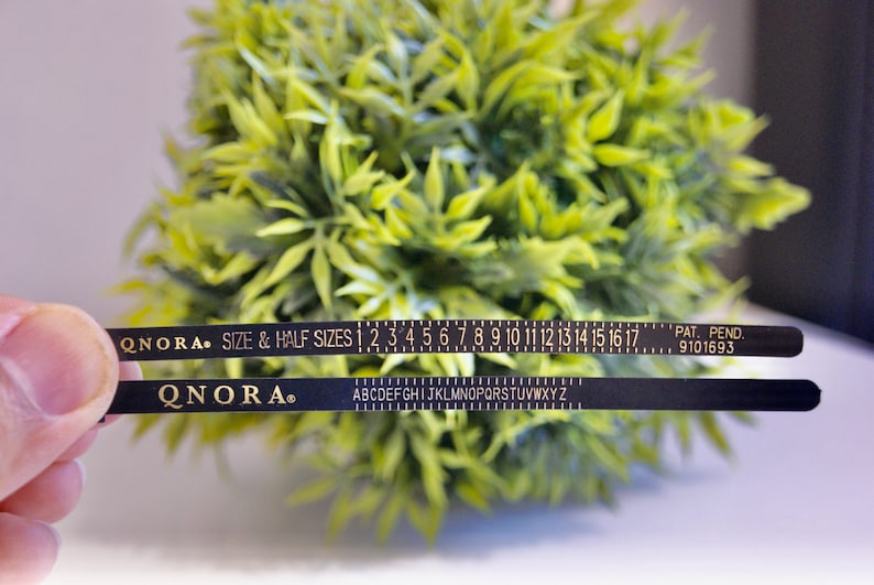 Pode incluir: Fita m&eacute;trica preta com letras douradas. A fita tem uma r&eacute;gua com os n&uacute;meros de 1 a 17 e o alfabeto. O texto na fita diz "QNORA. SIZE & HALF SIZES 1 2 3 4 5 6 7 8 9 10 11 12 13 14 15 16 17 PAT. PEND. 9101693".