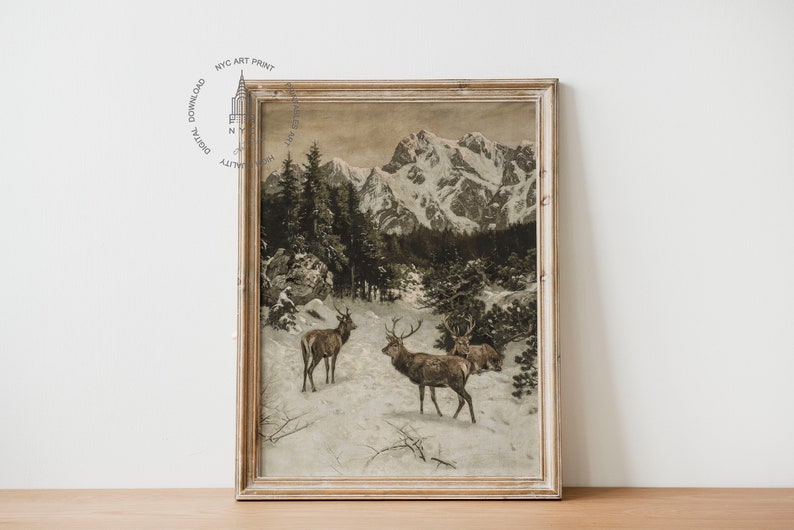 May include: A framed vintage print depicting a snowy mountain landscape with three deer in the foreground. The deer are brown and have antlers. The mountains are in the background and are covered in snow. The sky is a light blue colour.