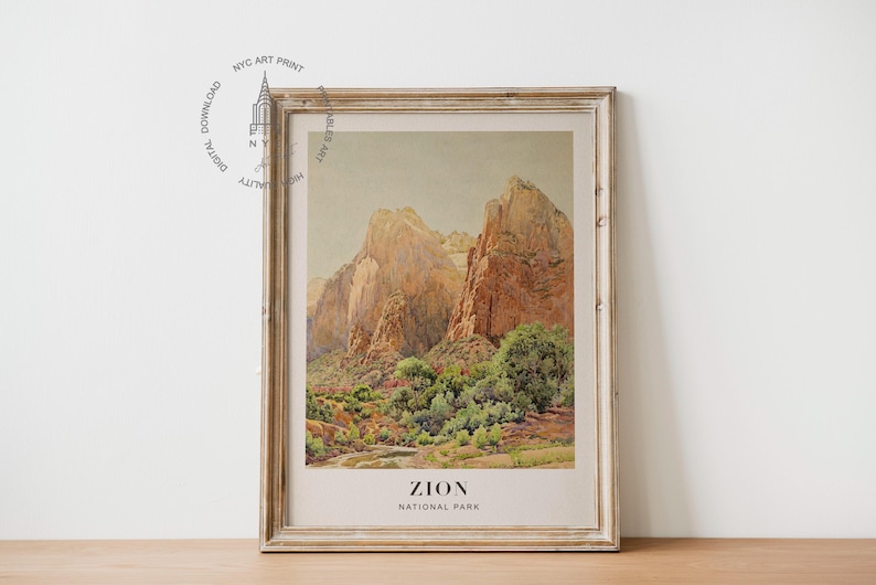 May include: Framed print of Zion National Park. The artwork depicts towering rock formations in shades of tan and brown, with green foliage at the base. The print is in a distressed, light-colored wooden frame. The text "ZION NATIONAL PARK" is at the bottom.