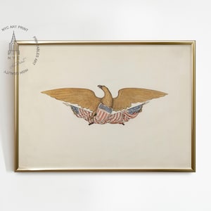 Op de afbeelding: Een ingelijste print met een gedetailleerde illustratie van een gouden adelaar met uitgespreide vleugels, die Amerikaanse vlaggen vasthoudt. Het kunstwerk is geplaatst tegen een cr&egrave;mekleurige achtergrond en ingelijst in een goudkleurige lijst. De print is gelabeld "NYC ART PRINT".