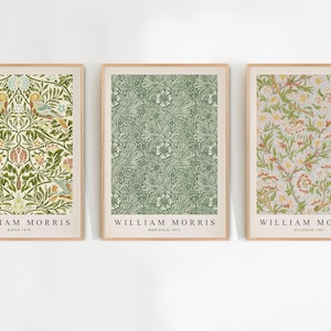 Op de afbeelding: Drie ingelijste prints van William Morris met bloemmotieven. De eerste print heeft een groen en wit bloemmotief met de tekst "William Morris, Bird 1875". De tweede print heeft een groen en wit bloemmotief met de tekst "William Morris, Marigold 1875". De derde print heeft een roze en wit bloemmotief met de tekst "William Morris, Bloom 1875".