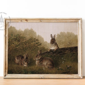 May include: A vintage painting of three brown rabbits in a forest setting. The rabbits are sitting on a log and in the undergrowth. The painting is framed in a light wood frame.