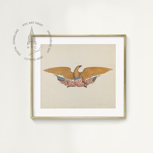 Op de afbeelding: Een ingelijste prent met een aquarelillustratie van een adelaar met uitgespreide vleugels. De adelaar is afgebeeld in bruin- en goudtinten, met een schild van rode, witte en blauwe strepen en sterren. De prent is ingelijst in een goudkleurige lijst.